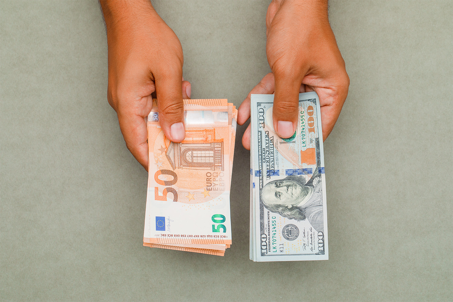 Imagem mostra mãos segurando cédulas de real e dólar